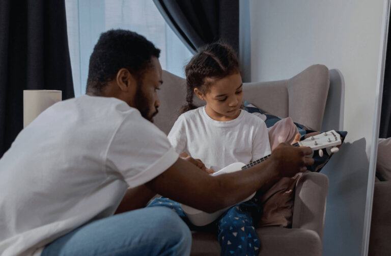 A father helping his little girl to play the guitar