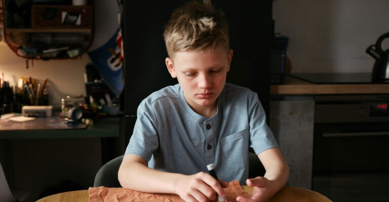 A young boy sitting at a table, looking down thoughtfully, with nothing in his hands.