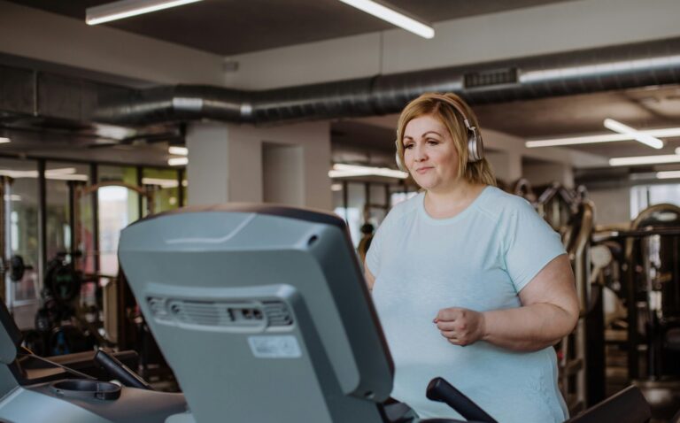 Woman with headphones walking on a treadmill in a modern gym, focused and wearing a light blue shirt