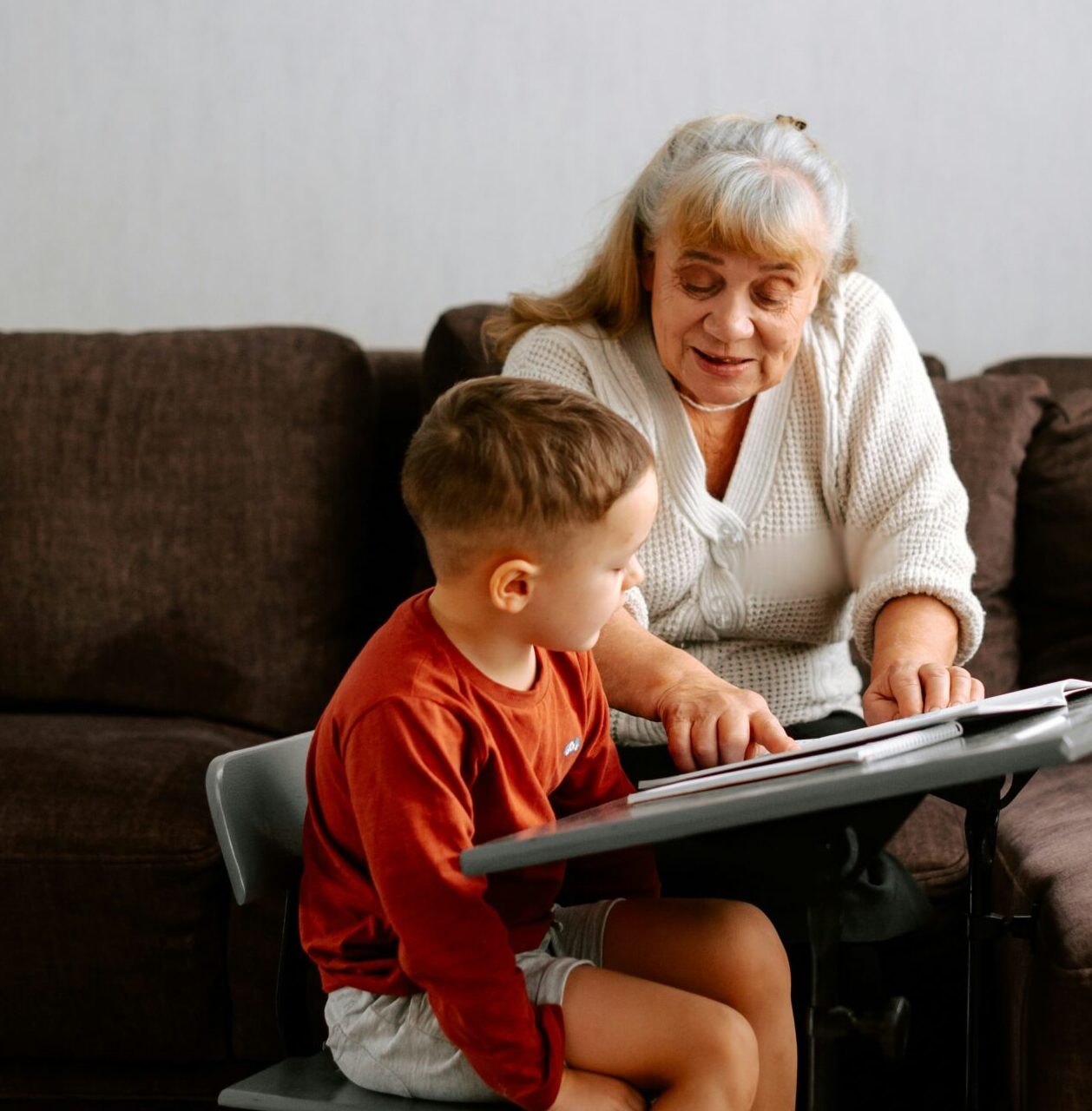 An elderly woman teaching a young boy at a table, both focused on a book.