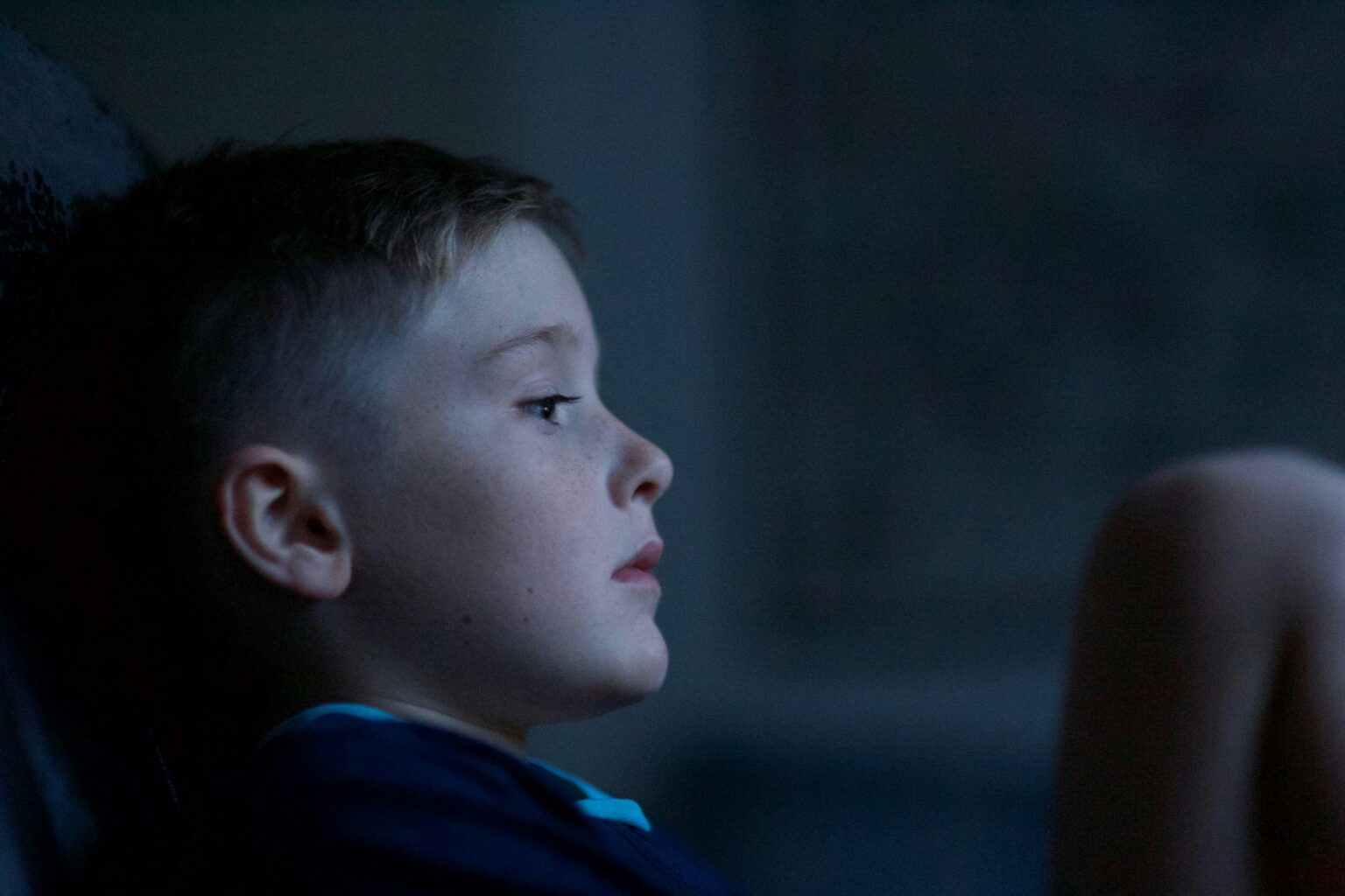 A side profile of a boy sitting in a dimly lit space, appearing thoughtful.