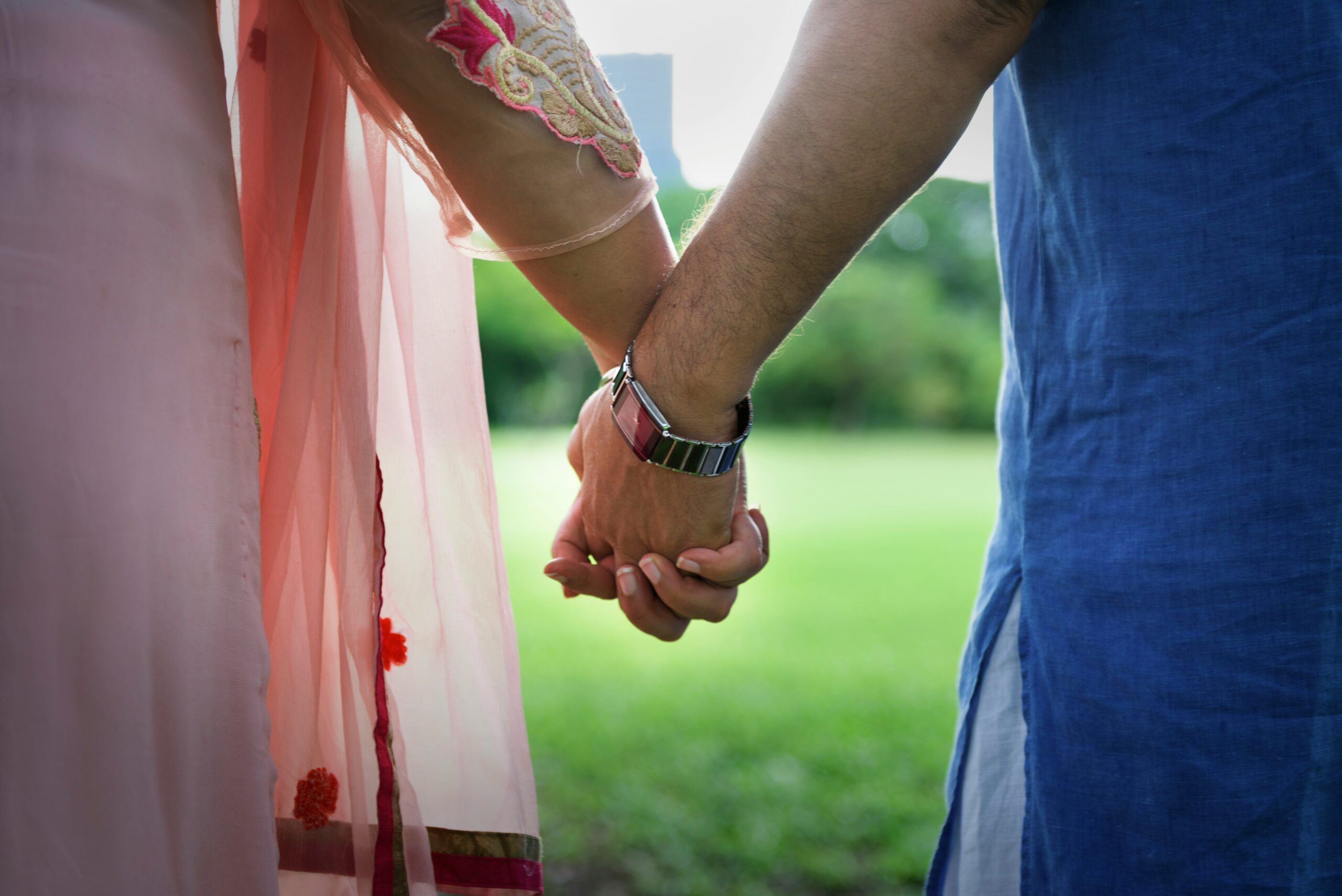 A heterosexual couple of south east asian descent, holding hands in a park.